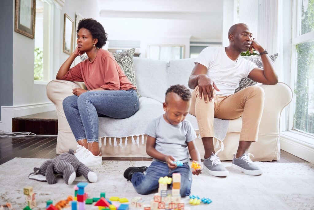 family, fight and couple argue on a sofa, stress and divorce with playing child on a living room floor. marriage, crisis and angry woman with man on couch after conflict, argument or problem with son