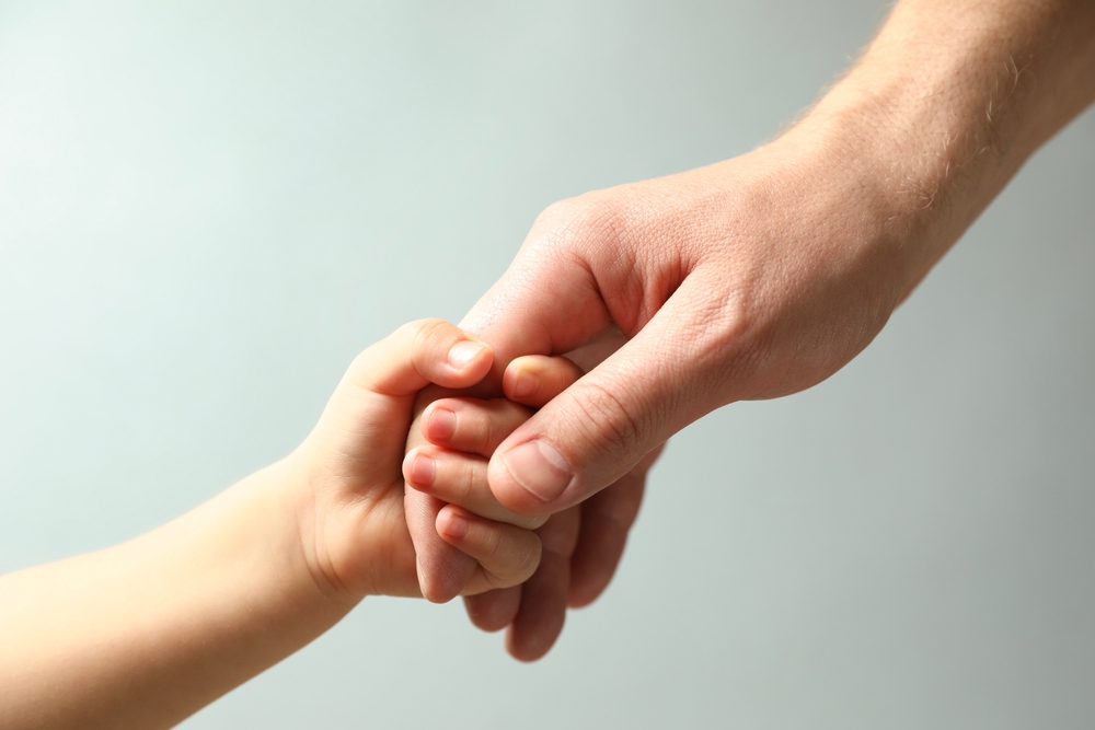 father,and,child,holding,hands,on,light,blue,background,,closeup